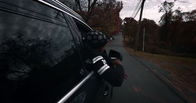 a man driving a car down a street next to a forest