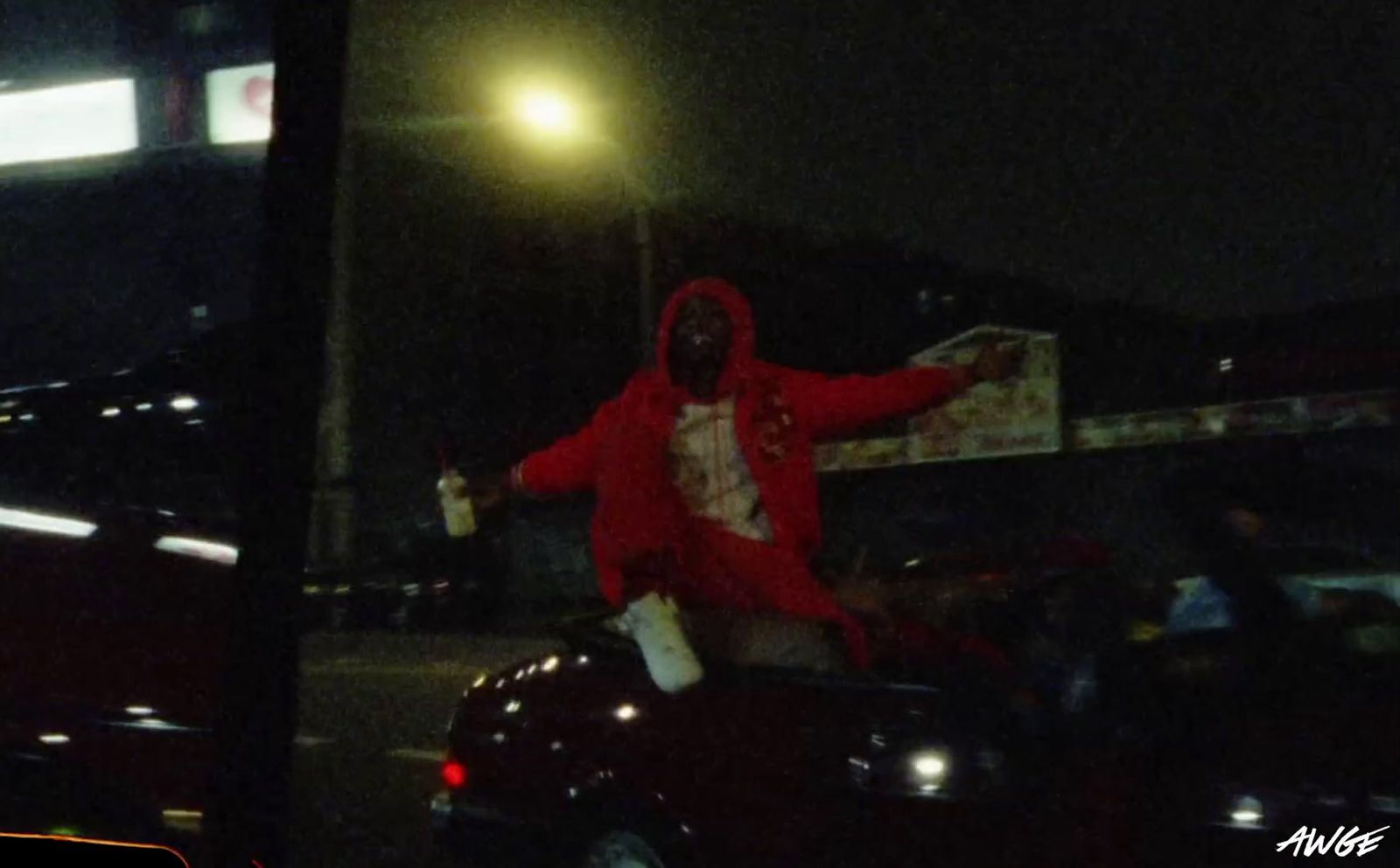 a man in a red hoodie standing on the back of a car