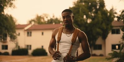 a man wearing a white tank top and brown suspenders