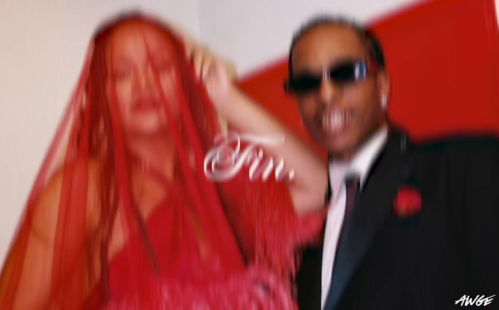 a man in a suit and sunglasses standing next to a woman in a red dress