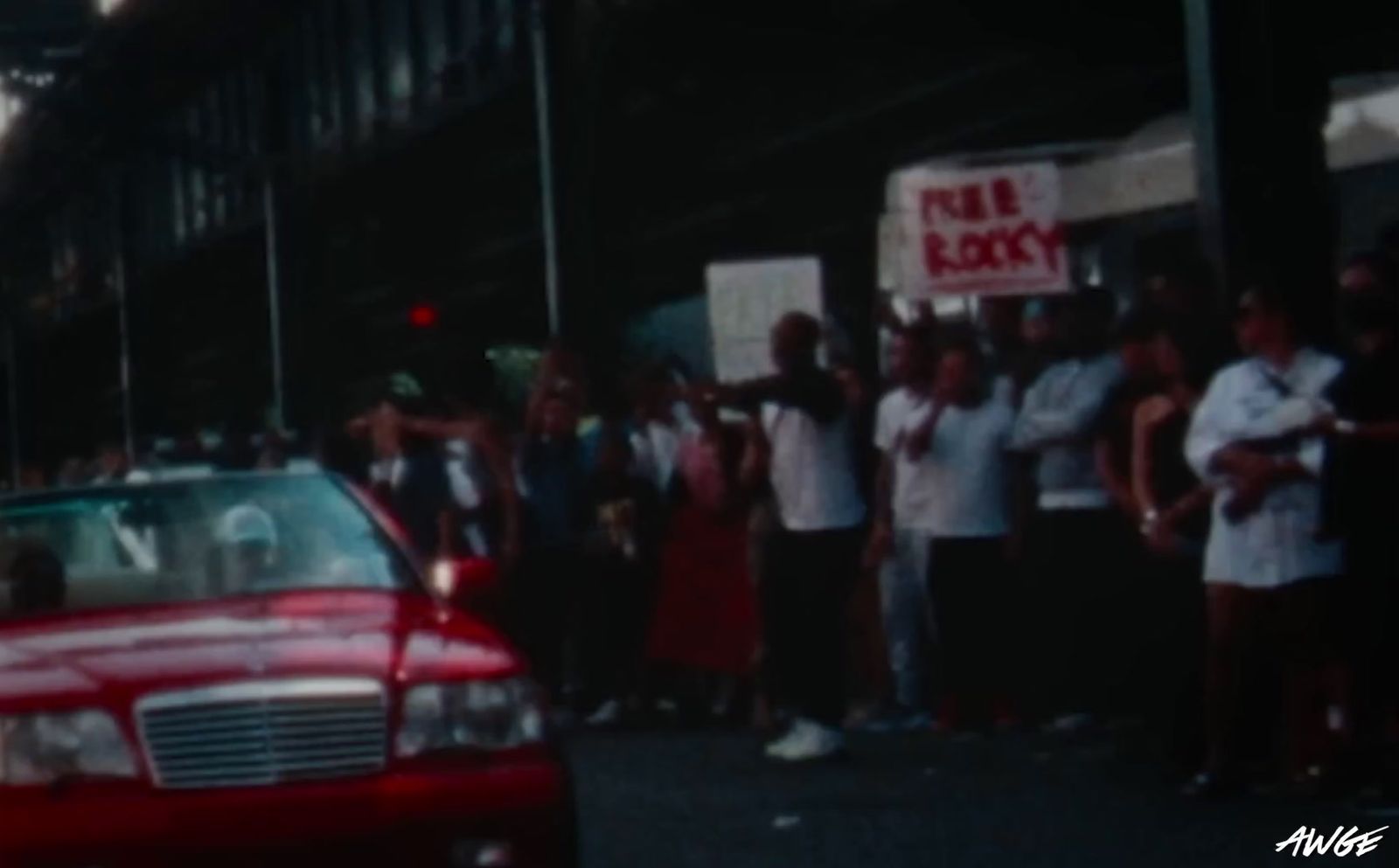 a red car driving past a crowd of people