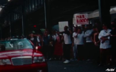 a red car driving past a crowd of people