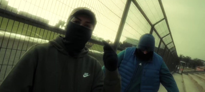 a couple of men walking down a street next to a fence