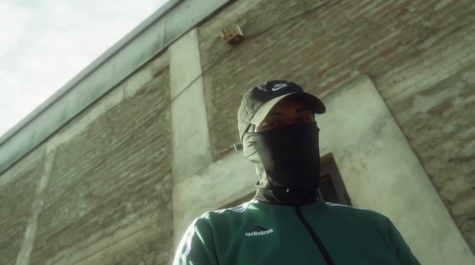 a man wearing a face mask standing in front of a brick building