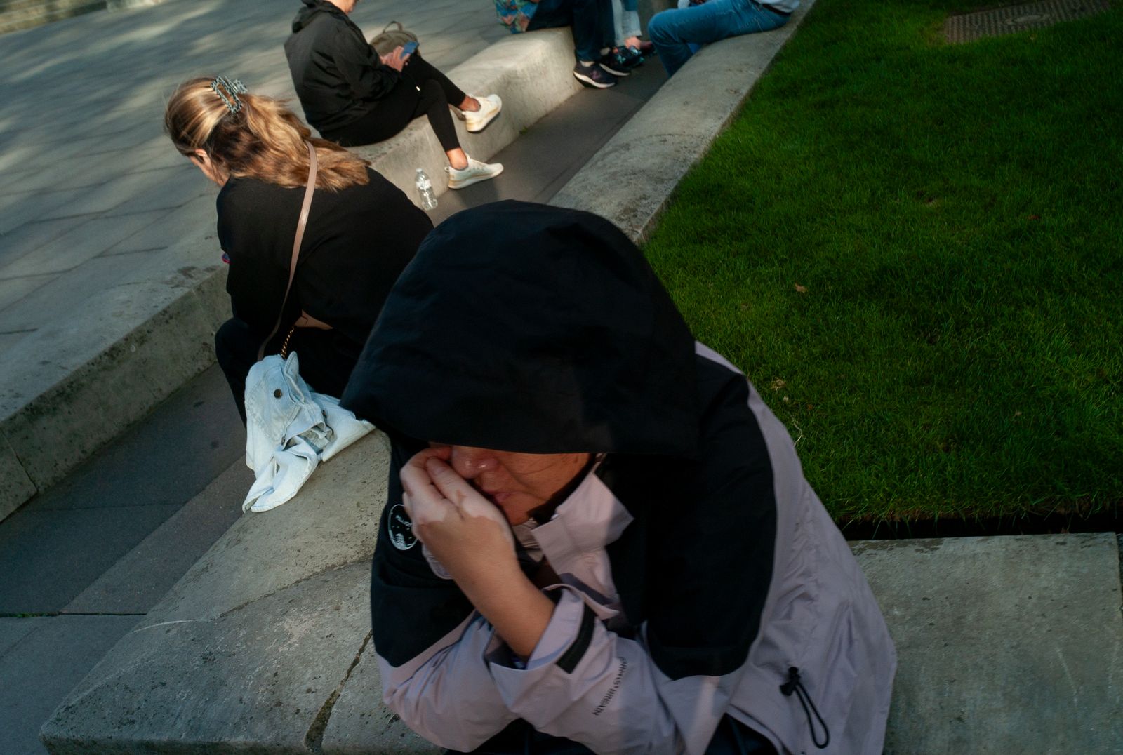 a group of people sitting on the side of a sidewalk