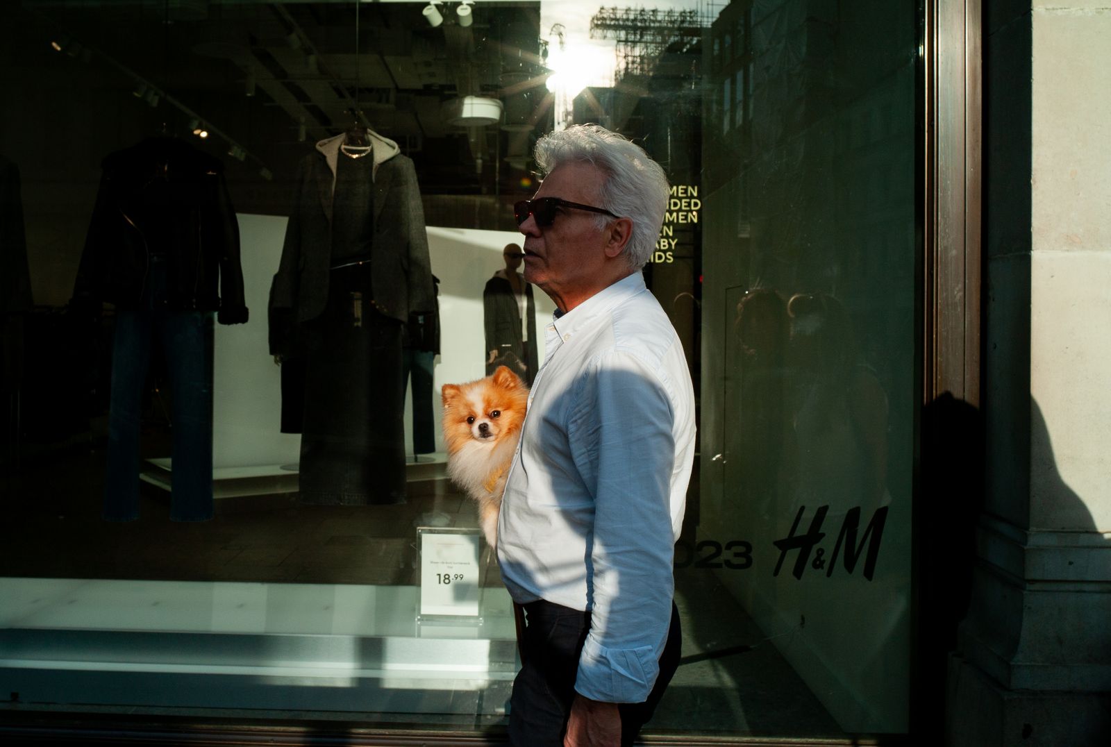 a man standing in front of a store window holding a small dog