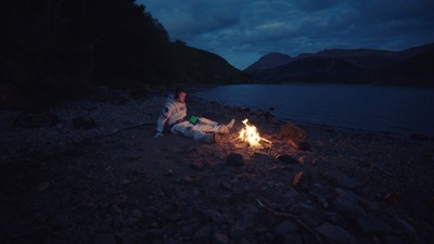 a man sitting next to a fire on a rocky beach