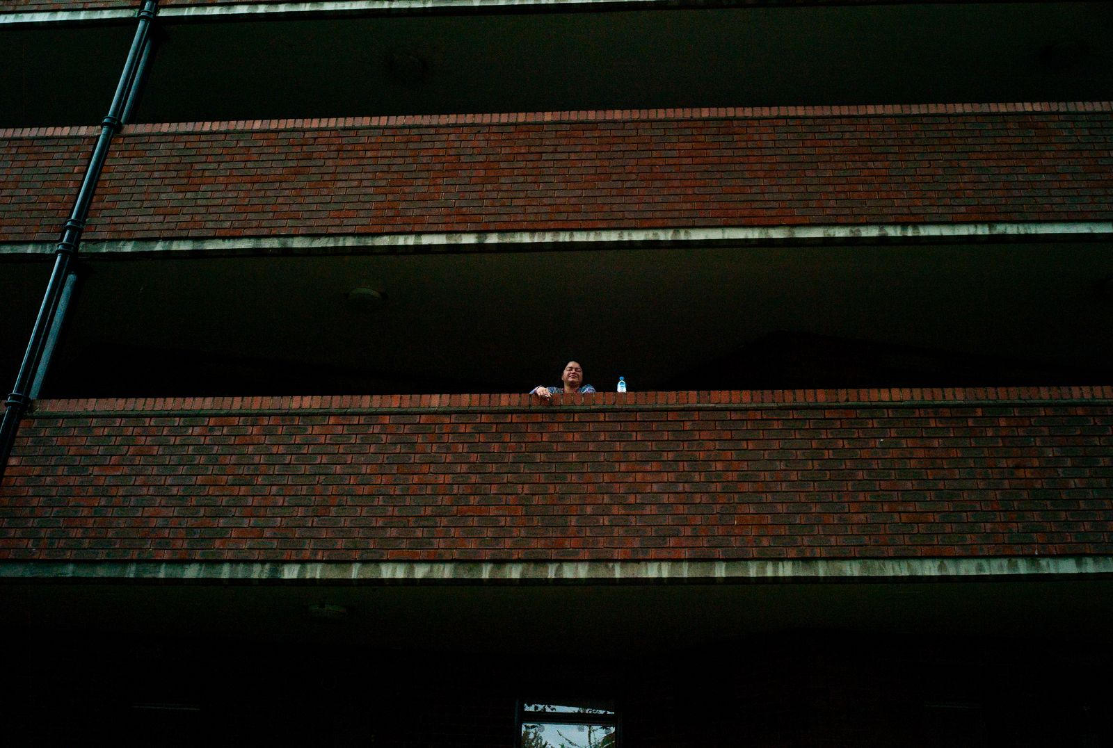 a woman standing on a balcony next to a brick building