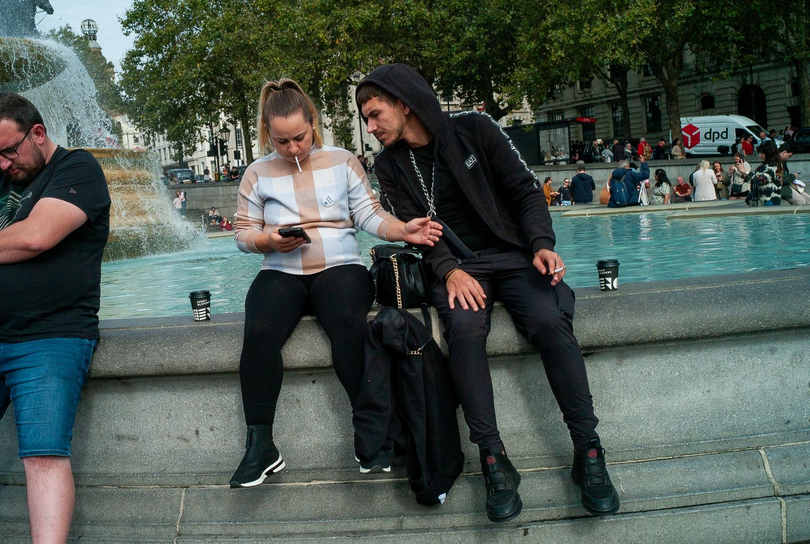 three people sitting on a fountain looking at a cell phone