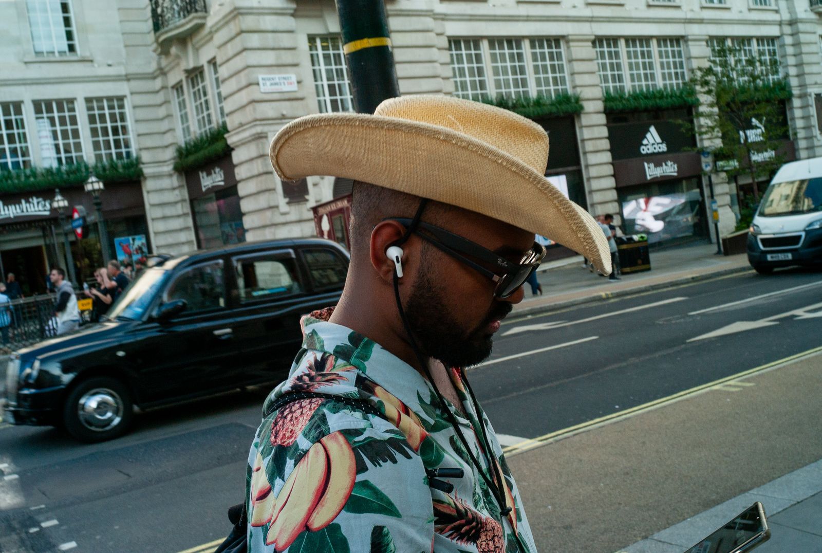 a man wearing a hat and glasses on a city street