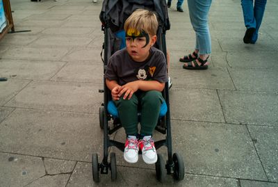 a young boy sitting in a stroller on a sidewalk