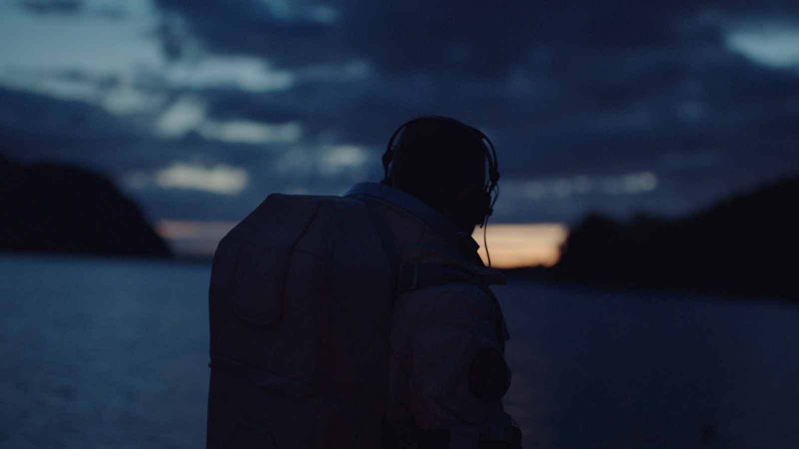 a man wearing headphones standing in front of a body of water