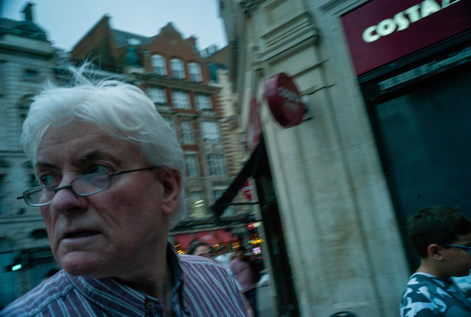 a man with white hair and glasses standing in front of a building