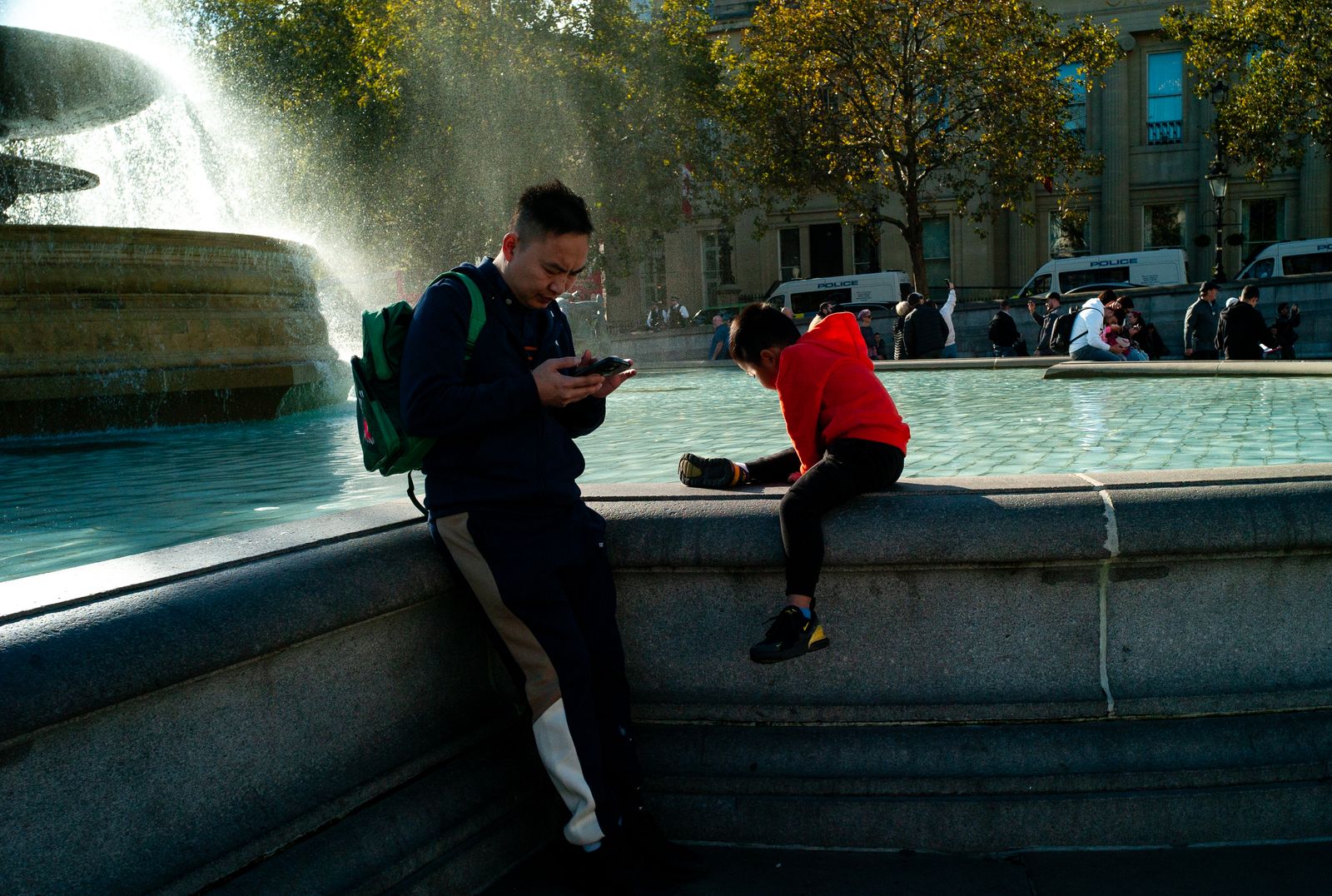 a man and a child sitting on a fountain looking at a cell phone