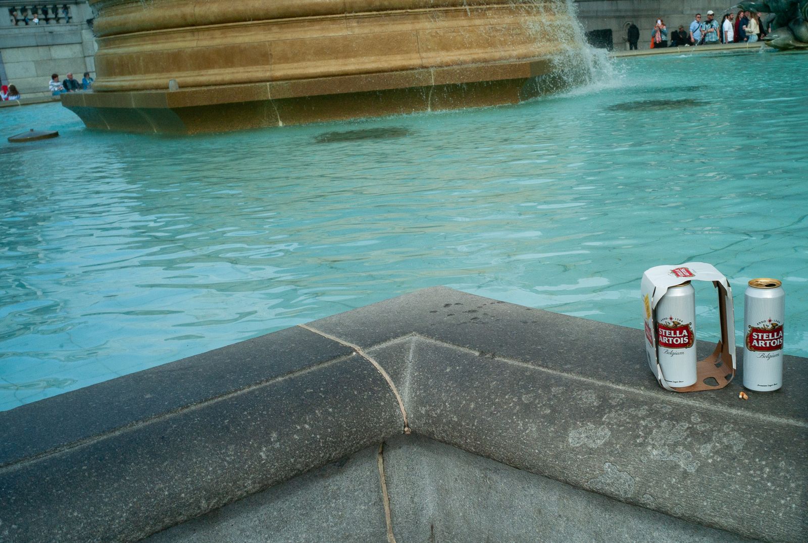 two cans of beer sitting next to a fountain