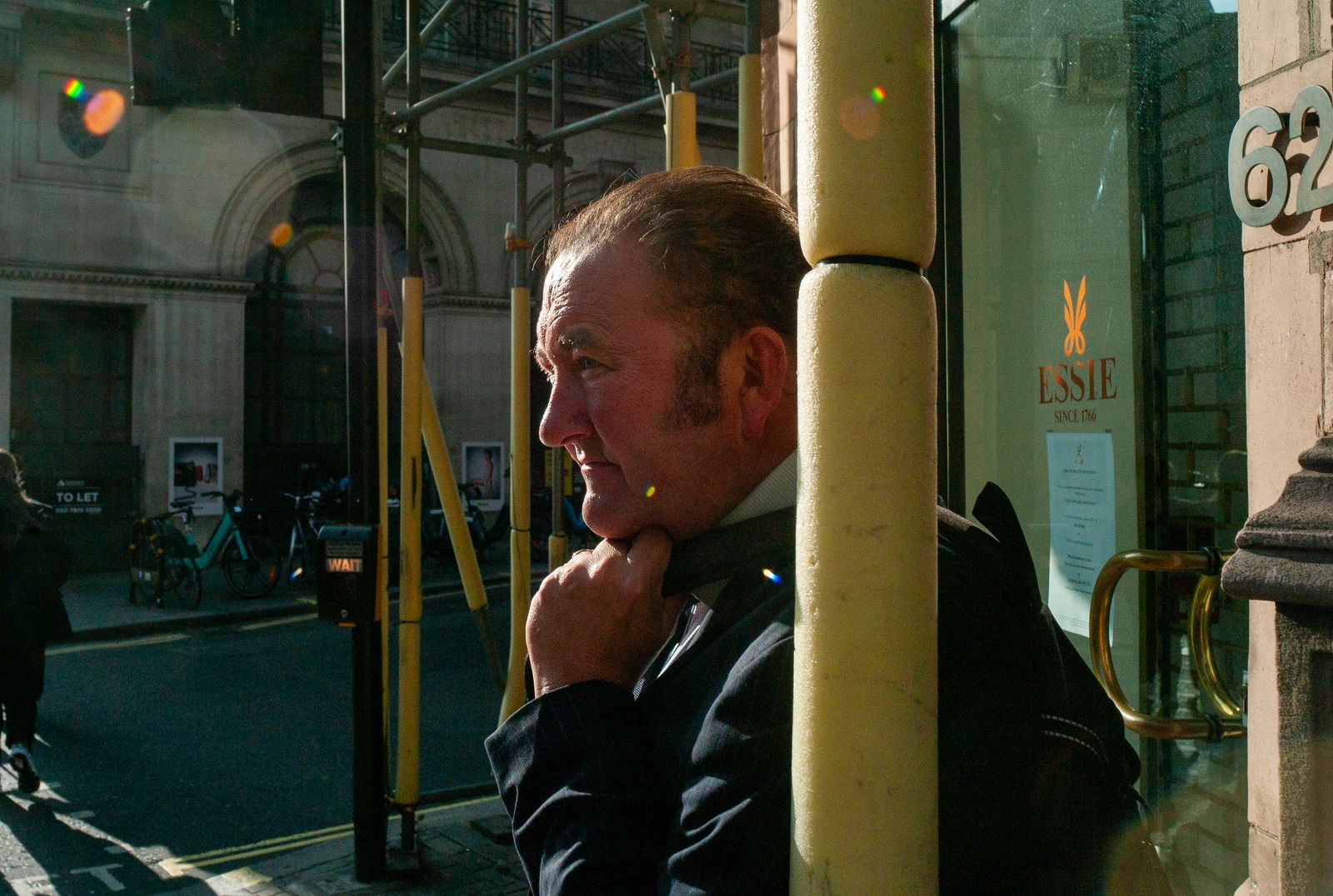 a man in a suit and tie leaning against a pole