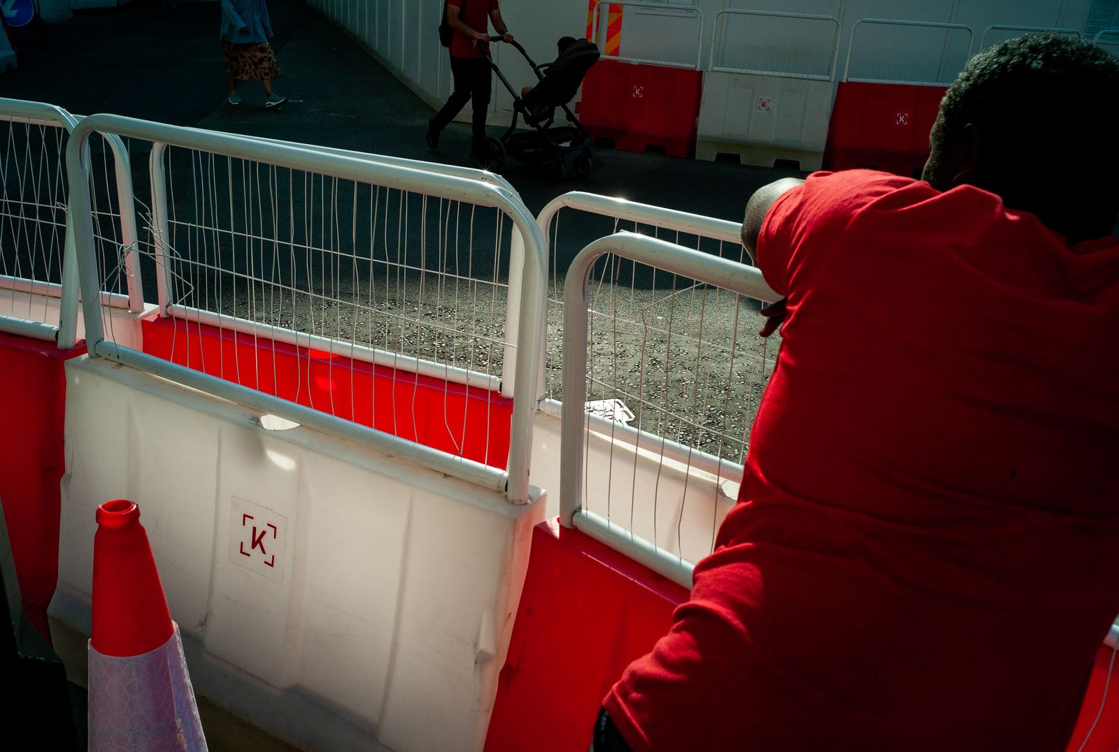 a person in a red hoodie leaning against a fence