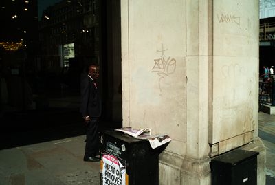 a man in a suit standing next to a trash can