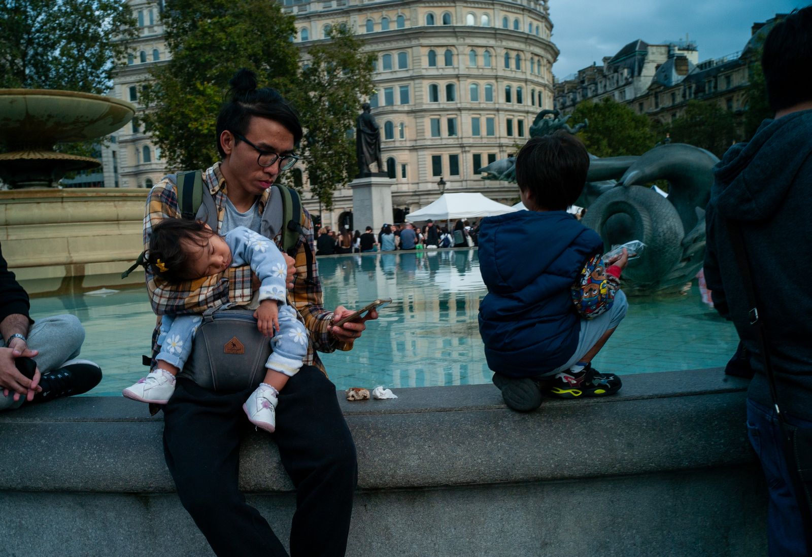 a man sitting next to a fountain holding a baby