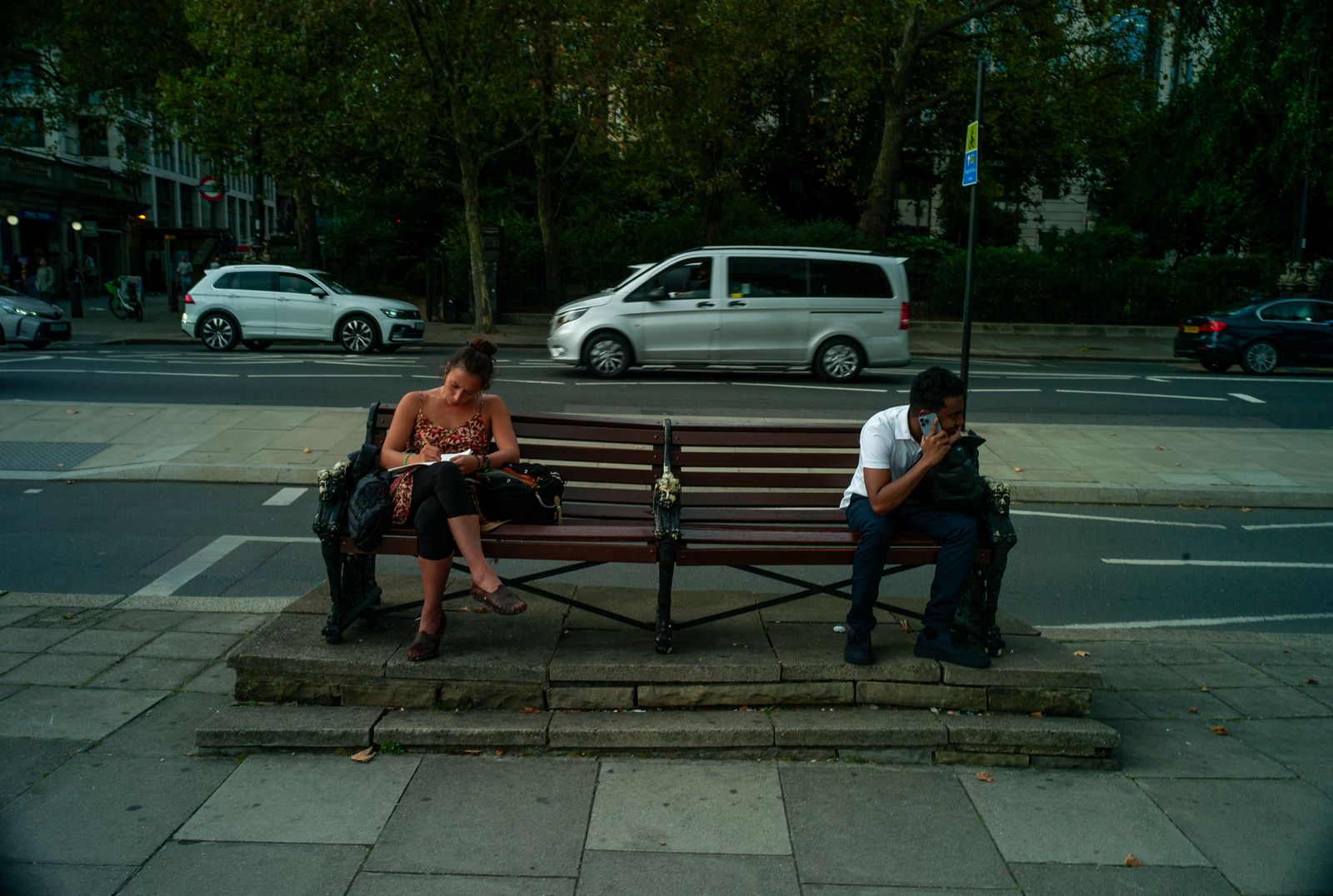 two people sitting on a bench on a city street