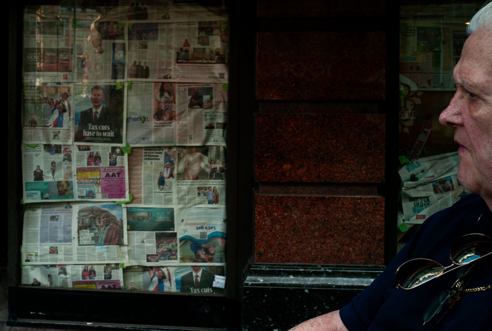 a man sitting on a bench in front of a newspaper stand