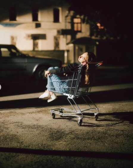 a woman sitting in a shopping cart on the side of the road