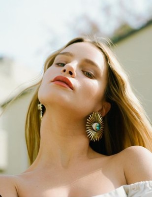 a woman in a white top is wearing a pair of earrings