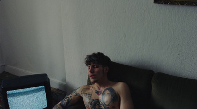 a man with tattoos sitting on a couch in front of a tv