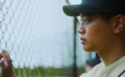 a young man holding a baseball bat next to a fence