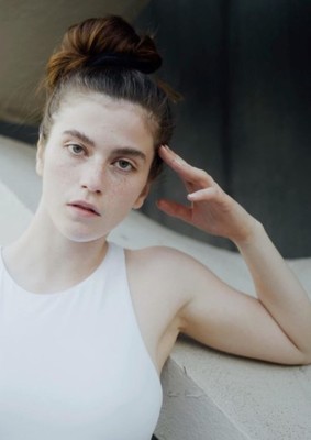 a woman in a white tank top leaning against a wall