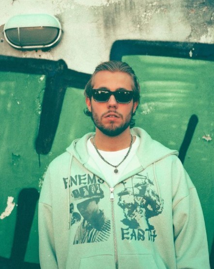 a man wearing sunglasses standing in front of a green wall