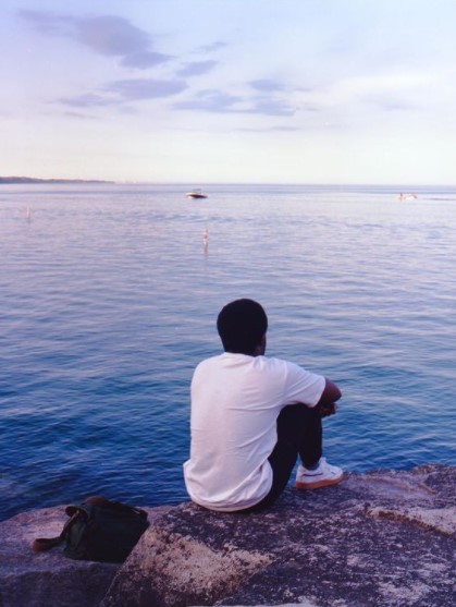 a man sitting on a rock looking out at the water