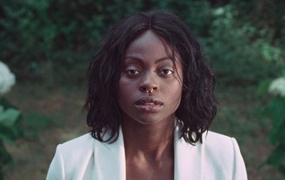 a woman in a white suit standing in front of a bush