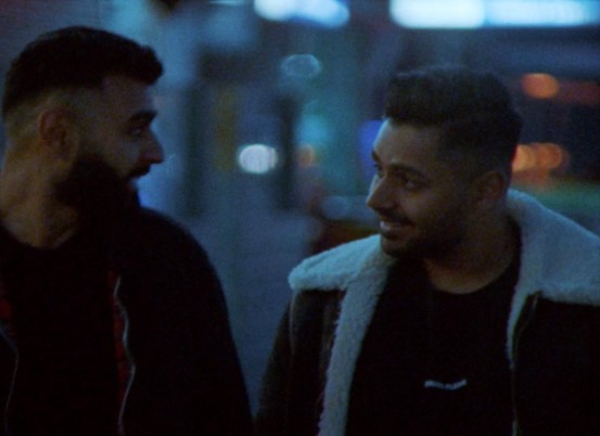 two men standing next to each other on a street