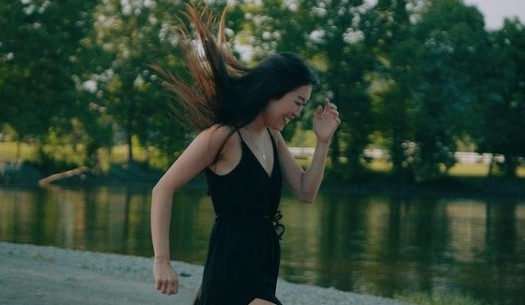 a woman in a black dress is running by the water