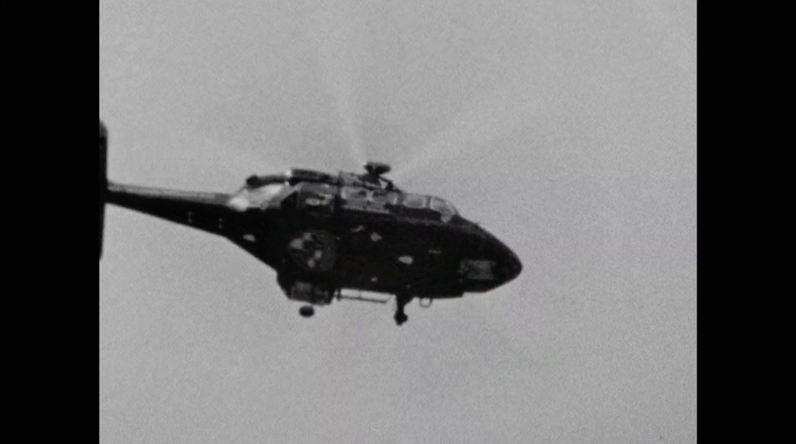 a black and white photo of a helicopter flying in the sky