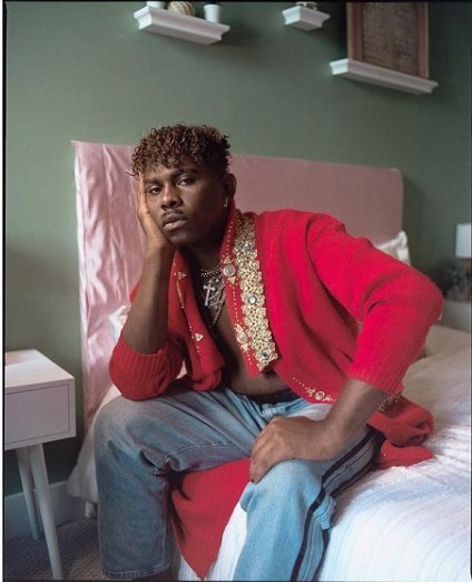 a man sitting on top of a bed in a red sweater