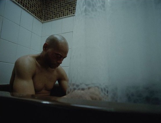 a bald man sitting in a bathtub with a shower head