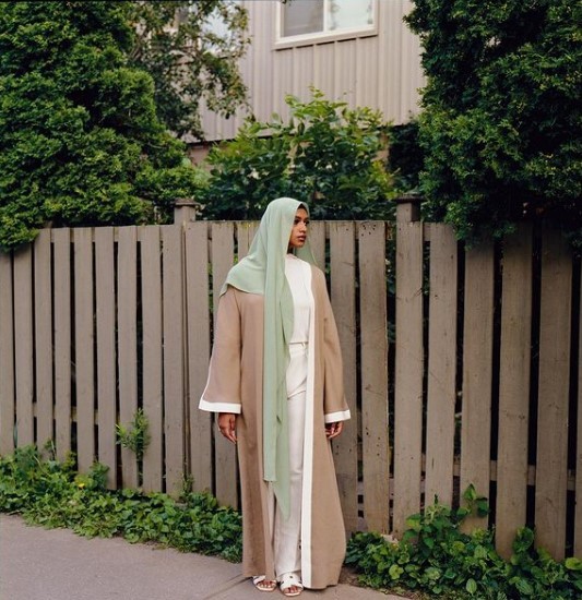 a woman standing on a sidewalk in front of a fence