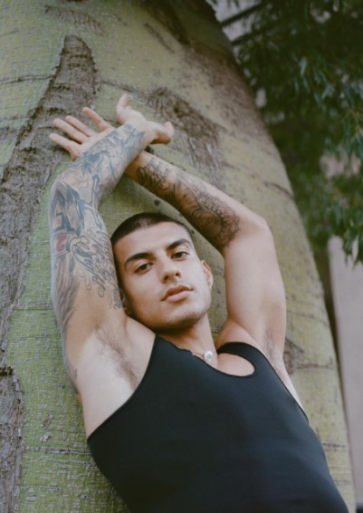 a man with a tattoo on his arm leaning against a tree