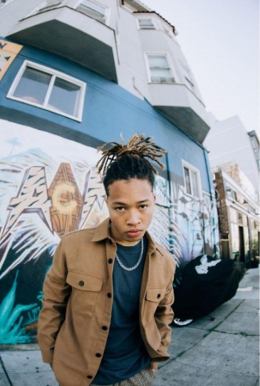 a man with dreadlocks standing in front of a building