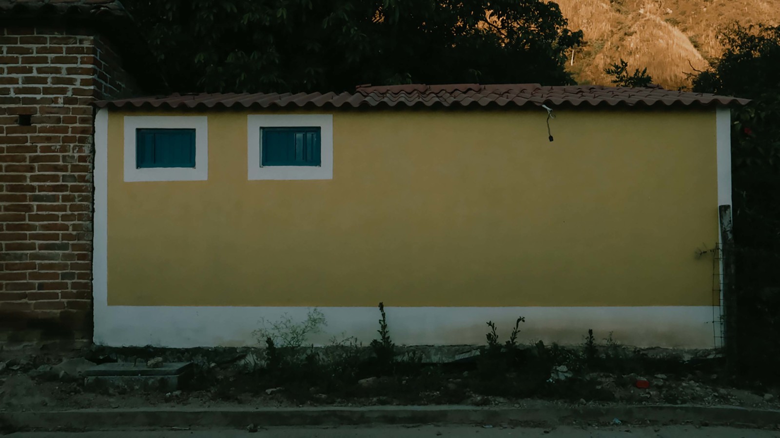 a yellow building with two windows and a red roof