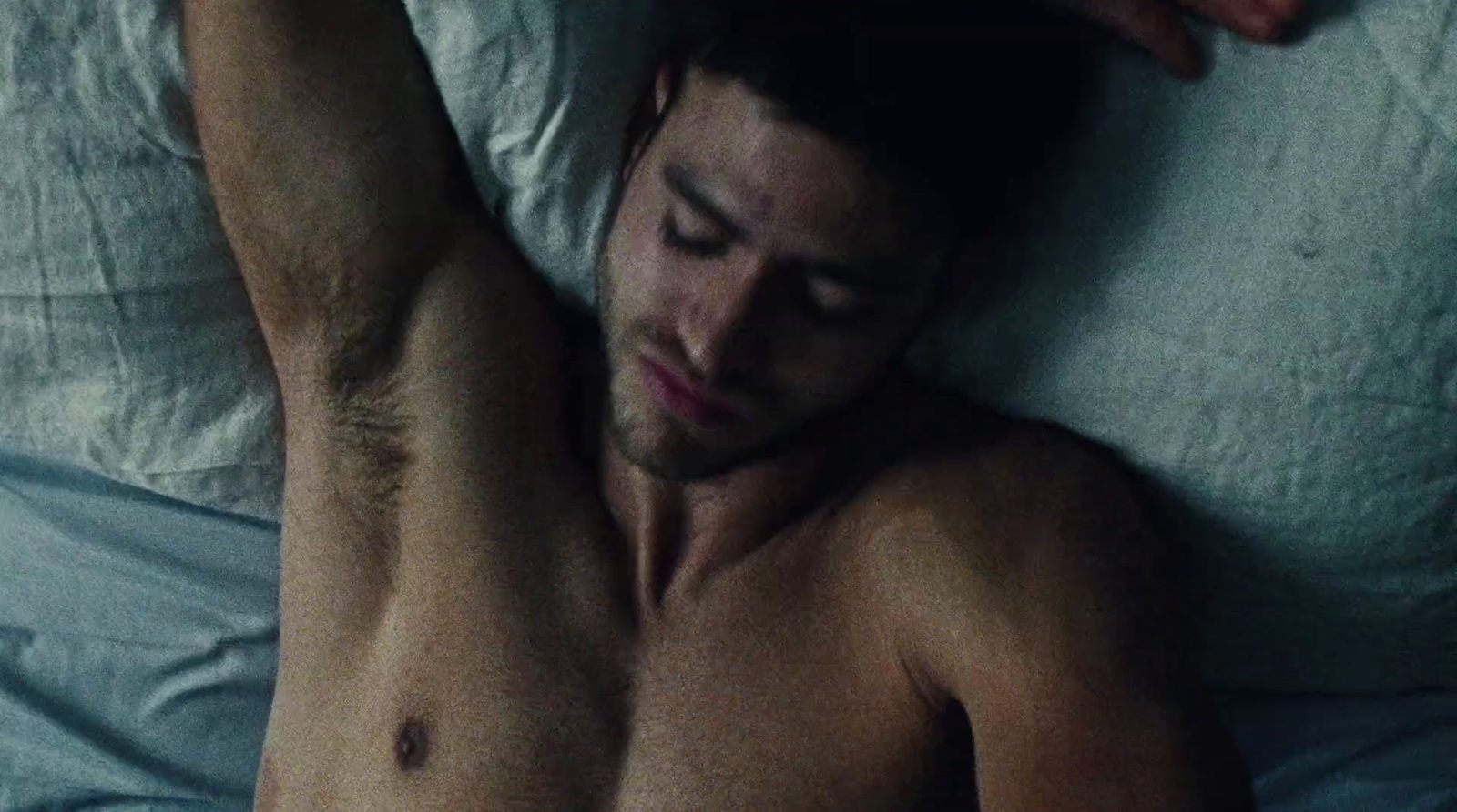 a shirtless man laying on a bed with his hands on his head