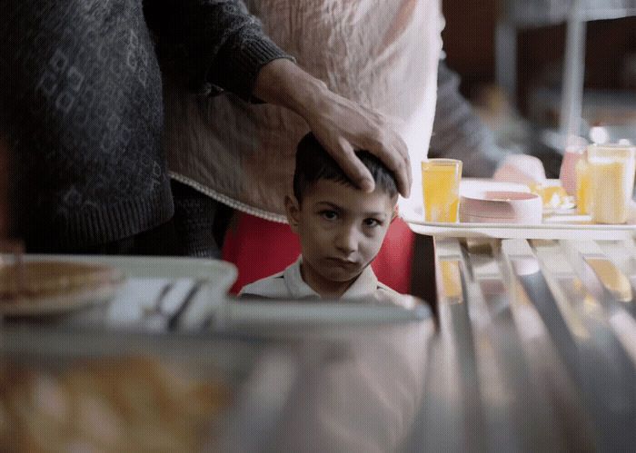 a young boy sitting at a table with a plate of food