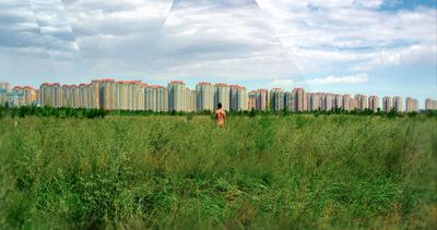 a man standing in a field with tall buildings in the background