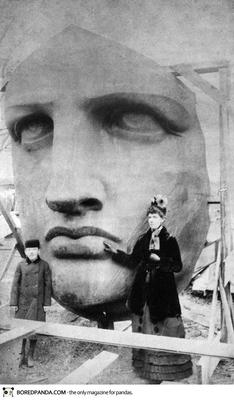 a woman standing next to a giant statue of a man