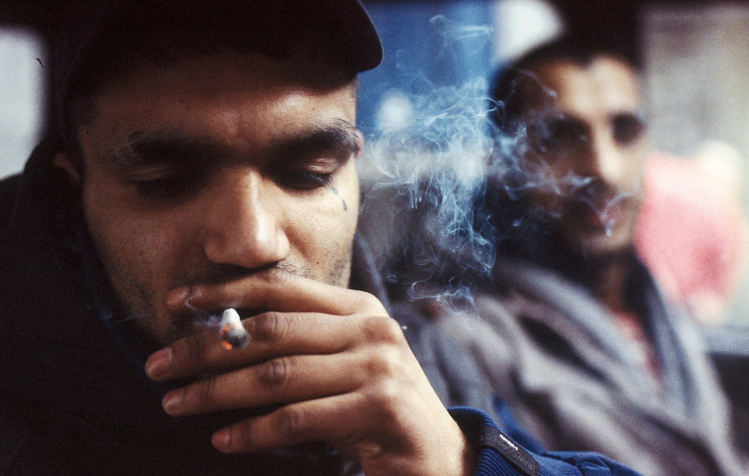 a man smoking a cigarette in front of another man