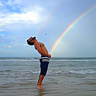 a man standing in the water with a rainbow in the background