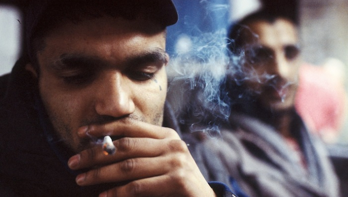 a man smoking a cigarette in front of another man