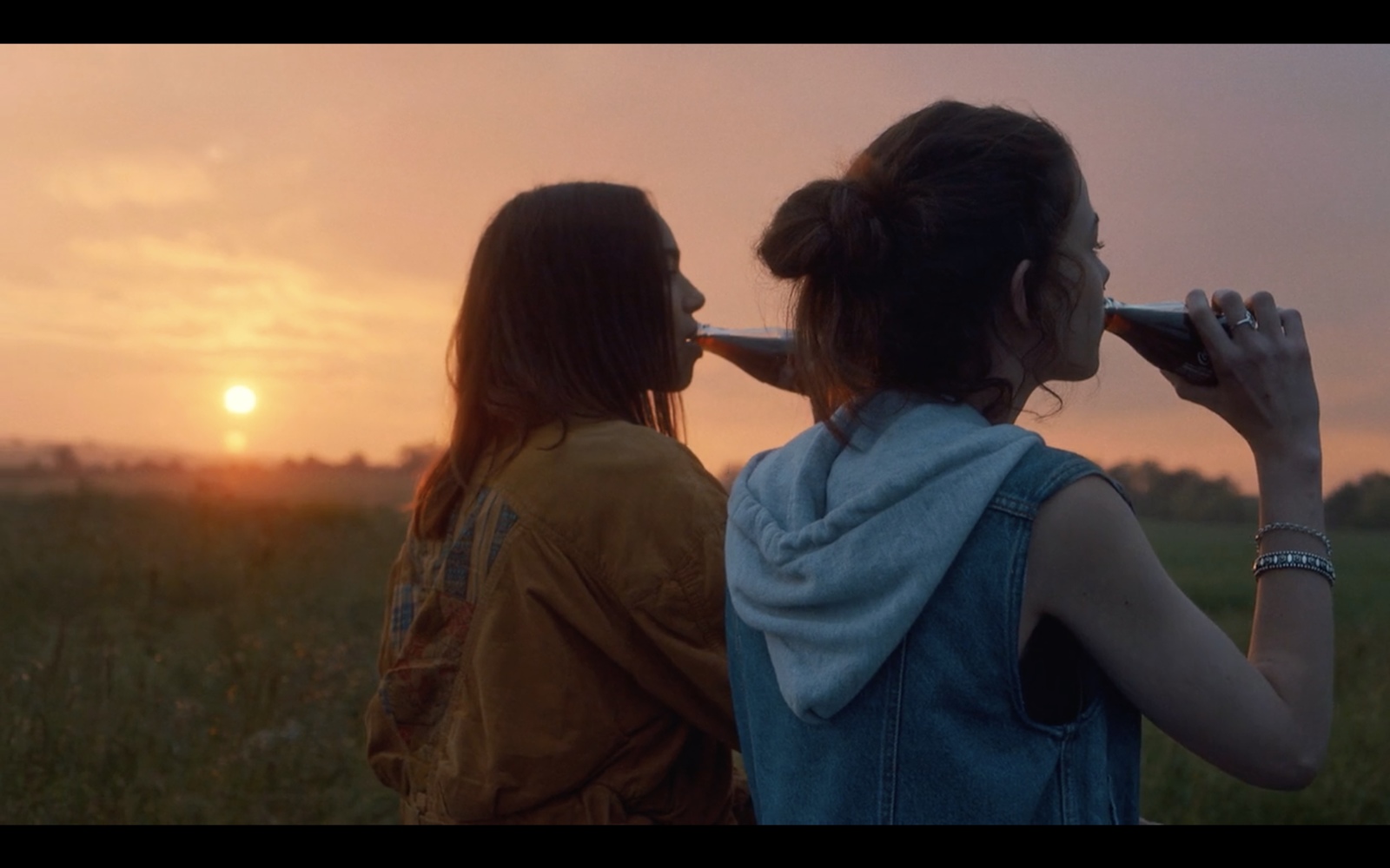 two girls are standing in a field watching the sun go down